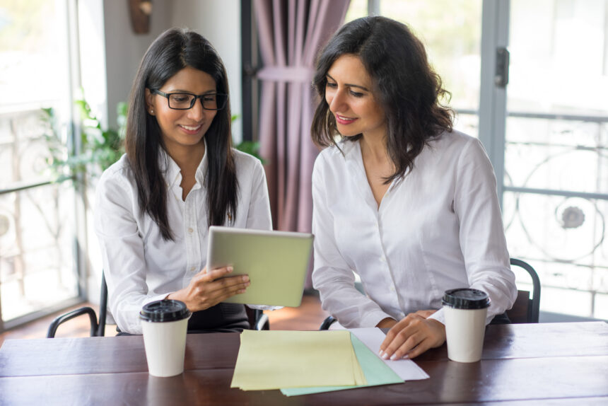 Smiling female business colleagues examining data on touchpad How to File a Complaint Against Online or Offline Service Providers in India